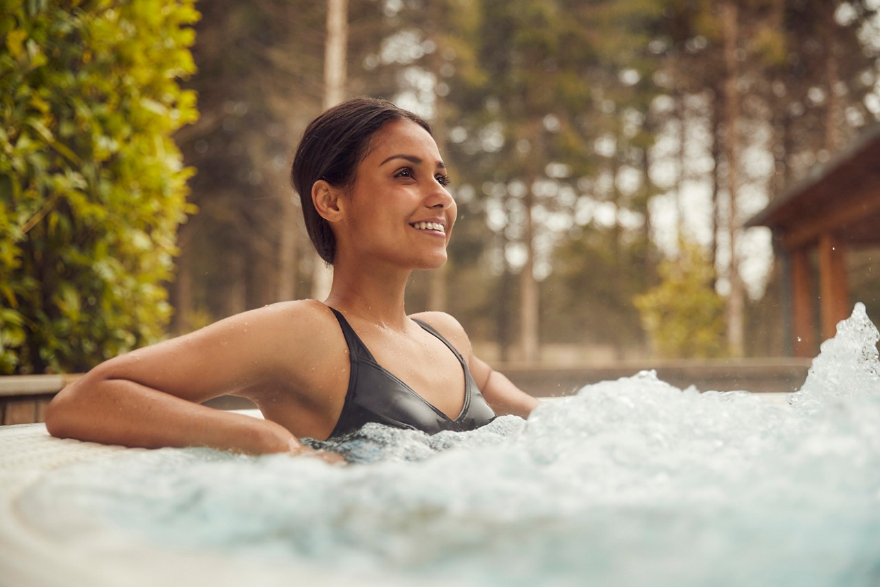 Woman soaking in a bubbling hot tub surrounded by the forest.